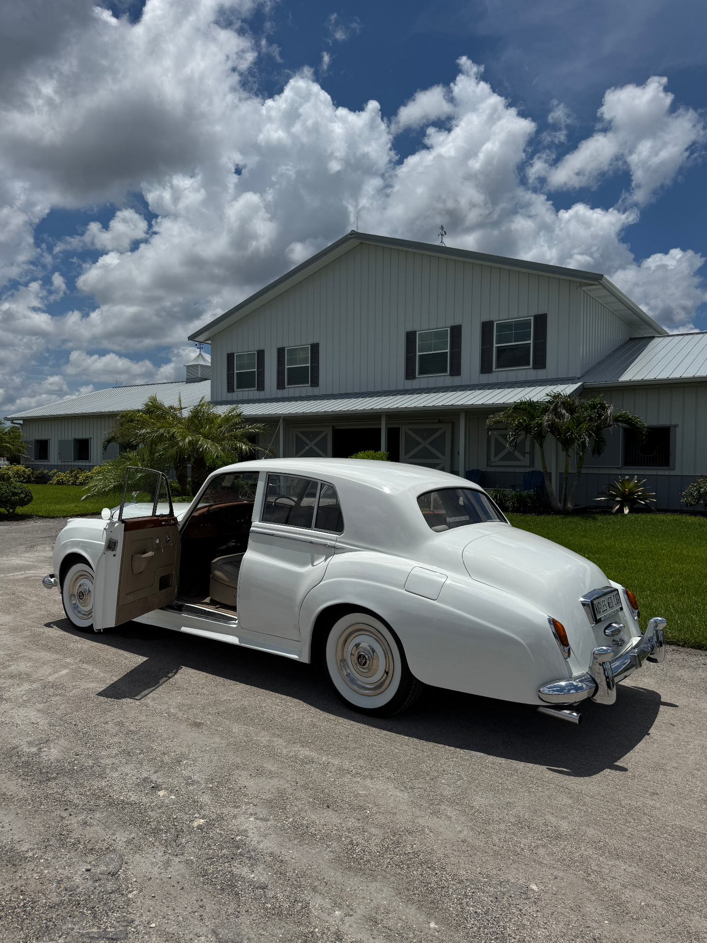 Vintage white Rolls-Royce Silver Cloud II wedding transportation with rear door open in front of a Southwest Florida equestrian barn